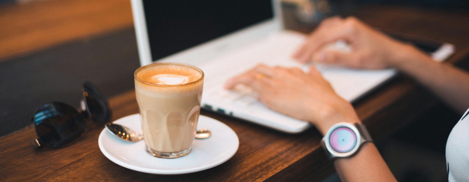 hands typing on a laptop beside a coffee